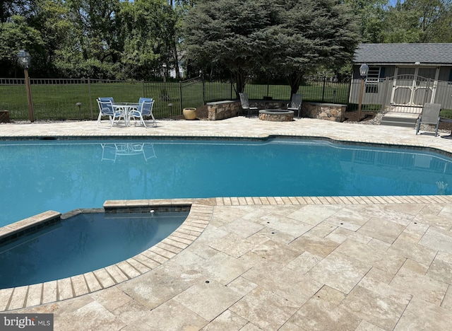 view of pool featuring a patio, a pool with connected hot tub, a yard, a fire pit, and fence