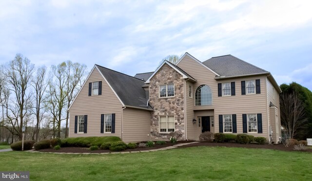 traditional-style house featuring a front yard, stone siding, and a shingled roof