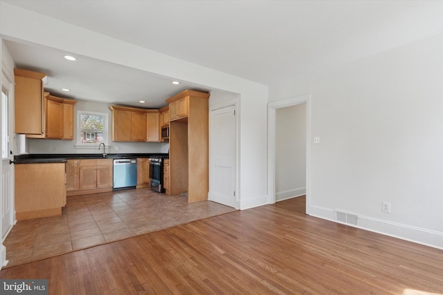 kitchen featuring recessed lighting, light wood-style flooring, stainless steel appliances, dark countertops, and a sink