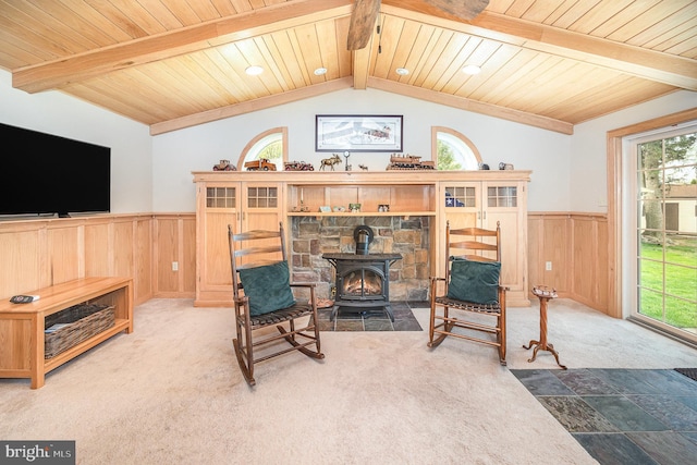 sitting room featuring a wood stove, vaulted ceiling with beams, wood ceiling, wainscoting, and carpet floors