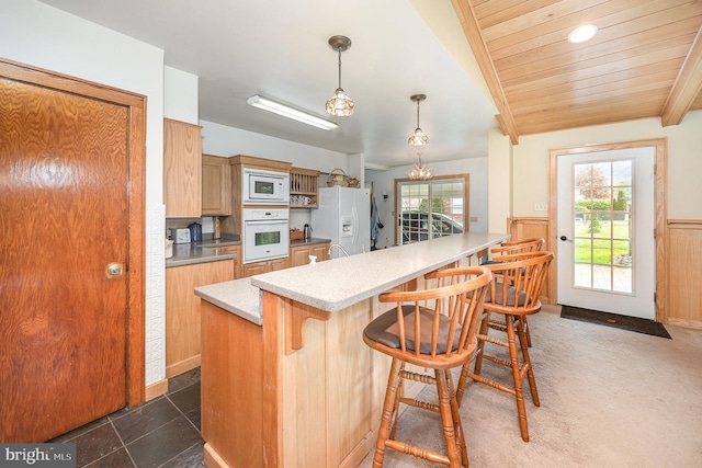 kitchen featuring pendant lighting, a breakfast bar area, light countertops, white appliances, and wainscoting