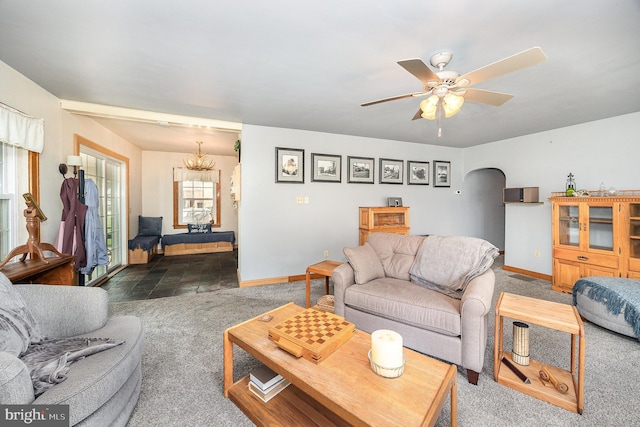 living area with arched walkways, carpet flooring, baseboards, and ceiling fan with notable chandelier