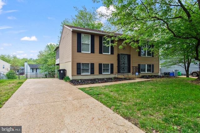 raised ranch featuring concrete driveway, fence, and a front lawn
