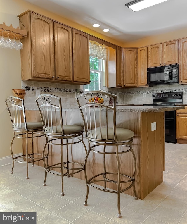 kitchen with a breakfast bar, tasteful backsplash, black appliances, and light tile patterned floors