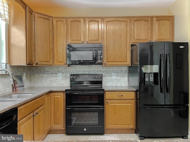kitchen with black appliances, decorative backsplash, light stone countertops, and a sink