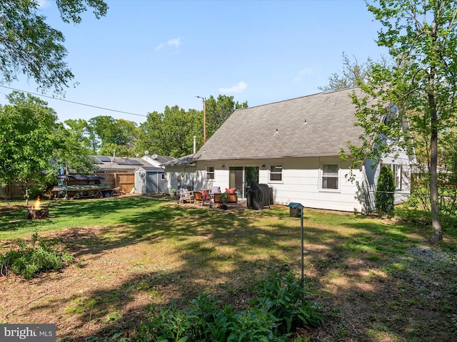 rear view of property featuring a fenced backyard, a lawn, an outdoor fire pit, and roof with shingles