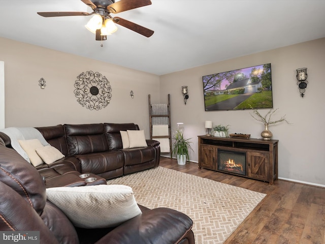 living area featuring baseboards, a ceiling fan, a glass covered fireplace, and wood finished floors