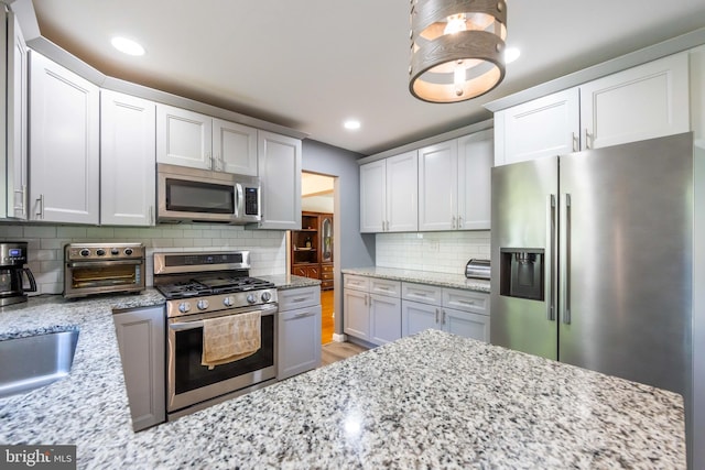 kitchen featuring light stone counters, stainless steel appliances, recessed lighting, light wood-type flooring, and backsplash