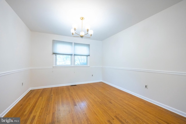 empty room featuring baseboards, a chandelier, and light wood finished floors
