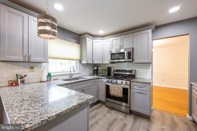 kitchen with decorative backsplash, light stone countertops, light wood-style floors, a sink, and stainless steel appliances