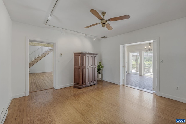 unfurnished room featuring track lighting, light wood finished floors, baseboards, a ceiling fan, and stairs