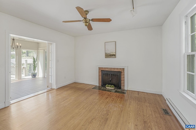 unfurnished living room with a baseboard heating unit, wood finished floors, a fireplace, a ceiling fan, and a chandelier
