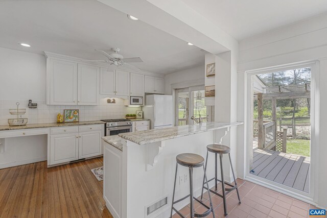 kitchen with white appliances, white cabinetry, plenty of natural light, a kitchen bar, and recessed lighting