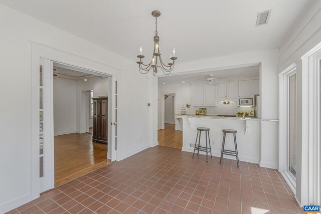 kitchen featuring a chandelier, decorative backsplash, a breakfast bar area, a peninsula, and white microwave