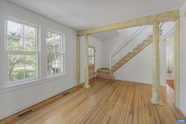 unfurnished living room with ornate columns, wood-type flooring, and stairway