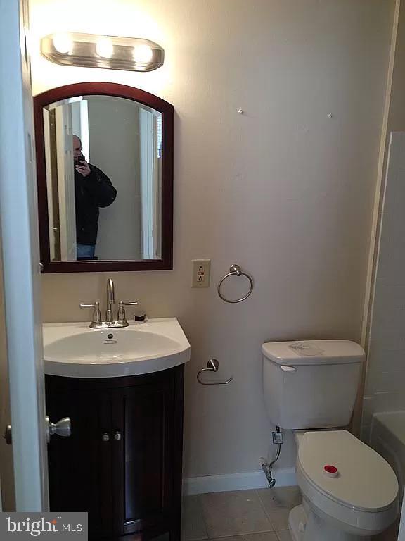 bathroom with a bathing tub, vanity, tile patterned floors, toilet, and baseboards