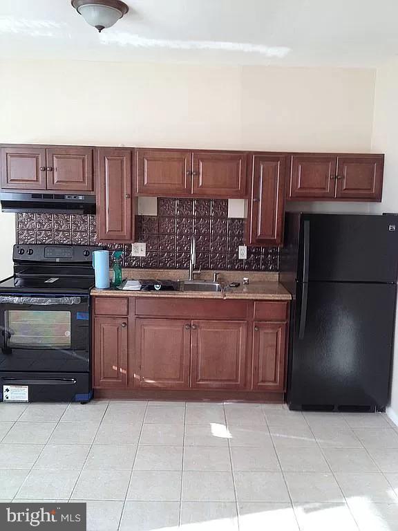 kitchen with a sink, under cabinet range hood, light tile patterned floors, black appliances, and backsplash