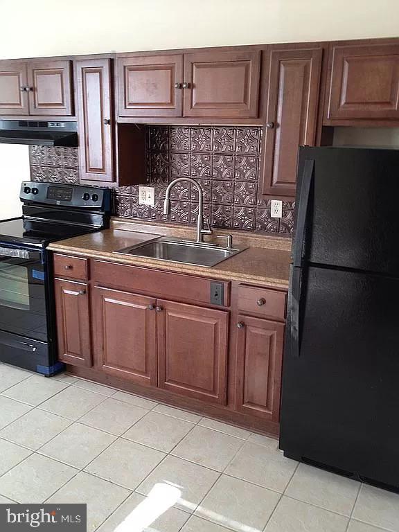 kitchen with tasteful backsplash, light tile patterned floors, under cabinet range hood, black appliances, and a sink