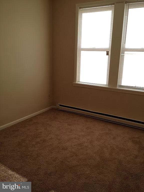carpeted spare room with a wealth of natural light, baseboards, and a baseboard heating unit