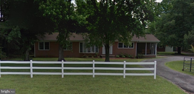 ranch-style house featuring brick siding, aphalt driveway, a front lawn, and a fenced front yard