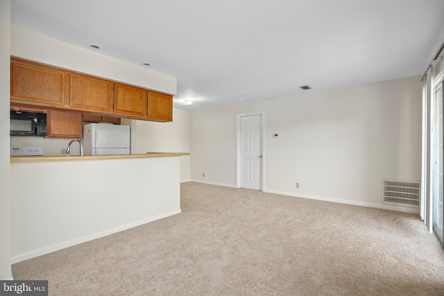 kitchen with black microwave, light carpet, freestanding refrigerator, baseboards, and visible vents