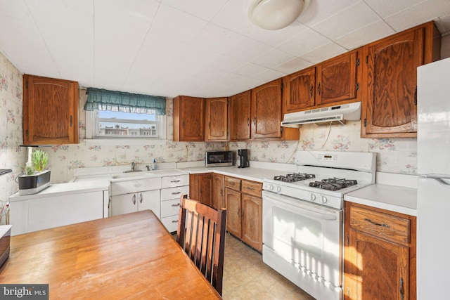 kitchen with white appliances, wallpapered walls, under cabinet range hood, and light countertops