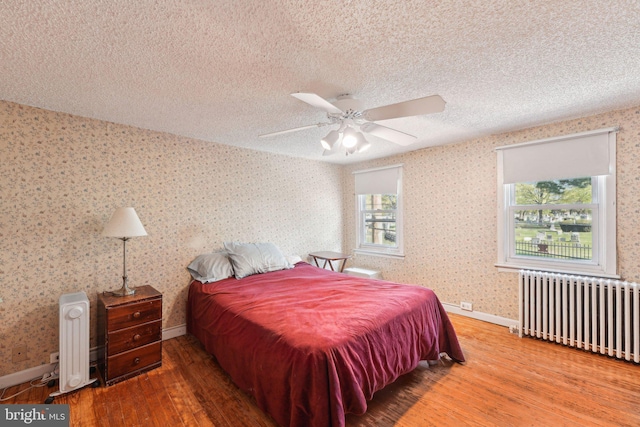 bedroom featuring radiator, a textured ceiling, wallpapered walls, and wood finished floors
