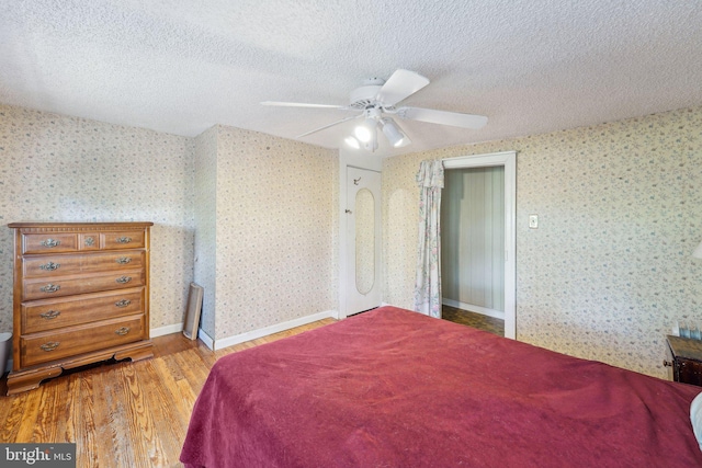 bedroom with a textured ceiling, wallpapered walls, a ceiling fan, and wood finished floors