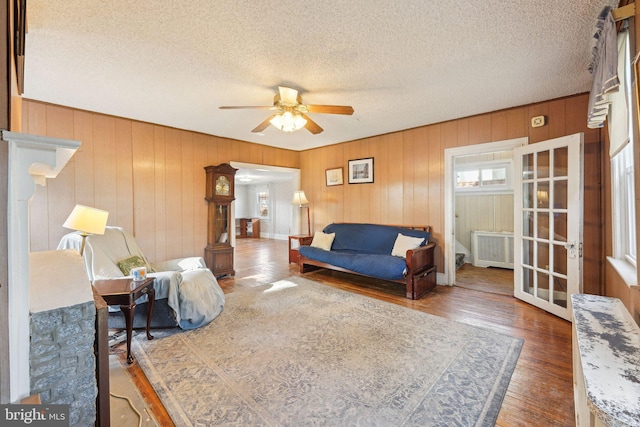 living room with wood walls, a textured ceiling, ceiling fan, and wood finished floors