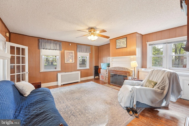 living room with ceiling fan, wood walls, wood finished floors, and radiator