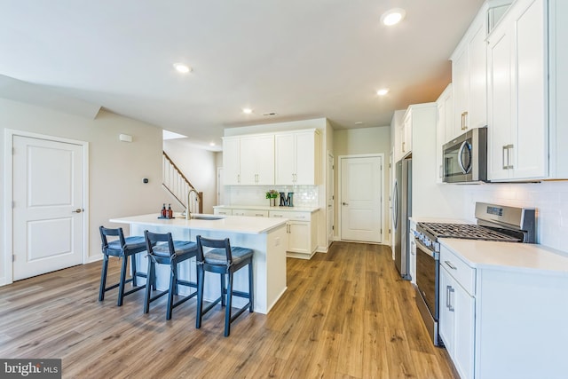 kitchen featuring a kitchen breakfast bar, a kitchen island with sink, appliances with stainless steel finishes, tasteful backsplash, and a sink
