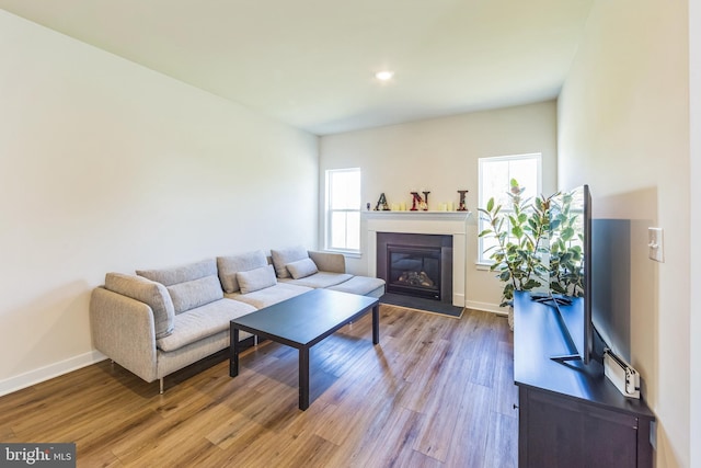 living area with baseboards, recessed lighting, a glass covered fireplace, and wood finished floors