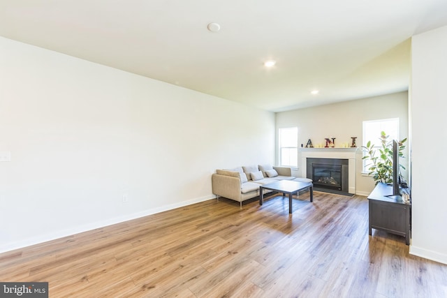 living area with a fireplace with flush hearth, baseboards, recessed lighting, and light wood-style flooring