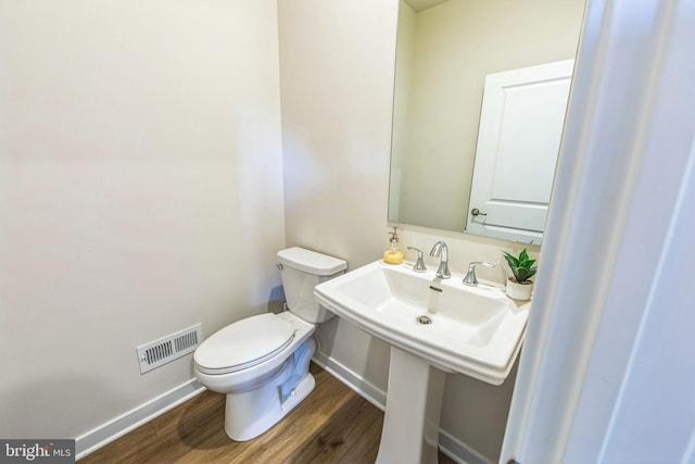 half bath featuring visible vents, baseboards, wood finished floors, and toilet