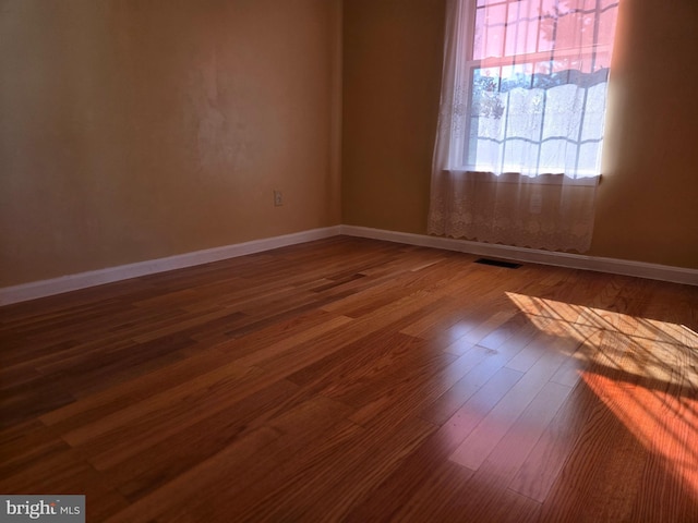 unfurnished room featuring visible vents, dark wood finished floors, and baseboards