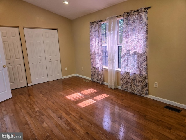 unfurnished bedroom with wood finished floors, two closets, baseboards, visible vents, and lofted ceiling