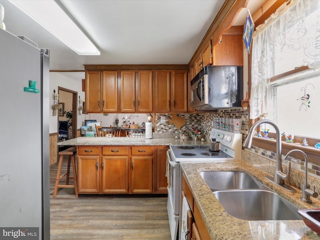 kitchen with brown cabinets, appliances with stainless steel finishes, a sink, a peninsula, and light wood-type flooring