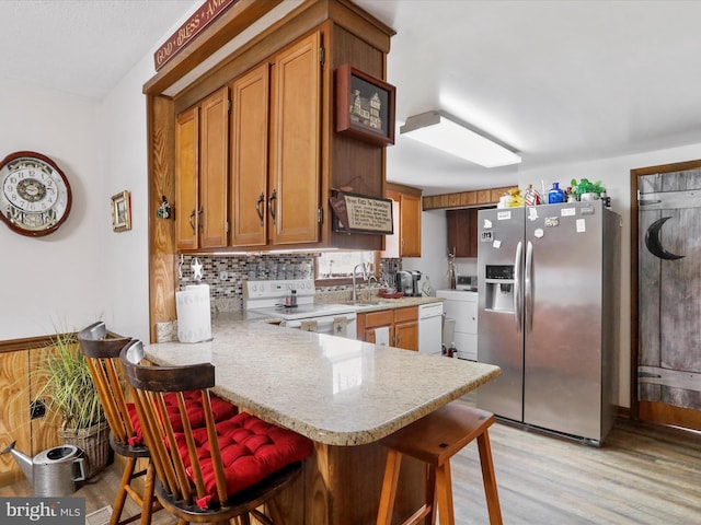 kitchen with light countertops, white electric range oven, brown cabinetry, and stainless steel refrigerator with ice dispenser