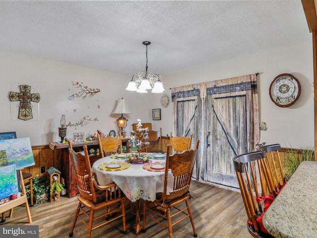 dining room with an inviting chandelier, a textured ceiling, wood finished floors, and wainscoting