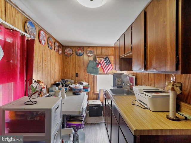 kitchen with a sink, brown cabinetry, light wood-type flooring, and wooden walls