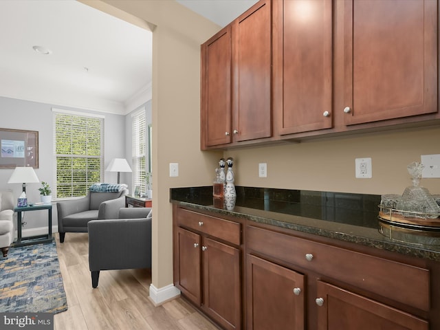 kitchen with brown cabinetry, light wood-style flooring, dark stone counters, open floor plan, and baseboards