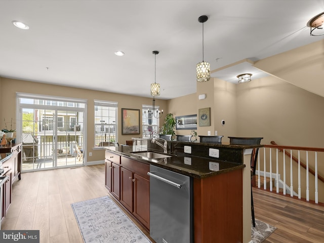 kitchen featuring stainless steel dishwasher, an island with sink, a breakfast bar area, a sink, and light wood-style flooring
