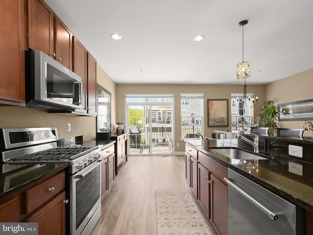 kitchen with pendant lighting, light wood-type flooring, a sink, an inviting chandelier, and stainless steel appliances