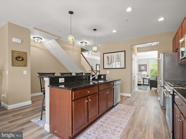 kitchen featuring appliances with stainless steel finishes, a breakfast bar area, dark stone countertops, and light wood-style flooring