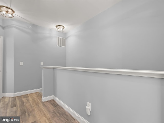 hallway with baseboards, visible vents, and wood finished floors