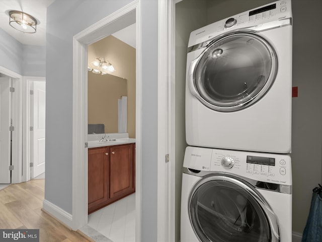 laundry room with laundry area, stacked washer and clothes dryer, light wood finished floors, and a sink