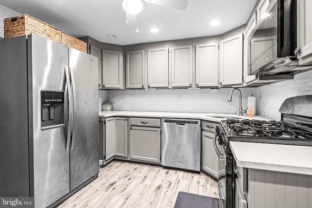 kitchen with stainless steel appliances, backsplash, light wood-style flooring, and a sink