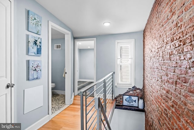 corridor featuring brick wall, an upstairs landing, visible vents, baseboards, and wood finished floors