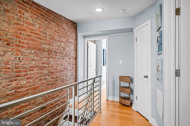 corridor with an upstairs landing, brick wall, light wood finished floors, and baseboards