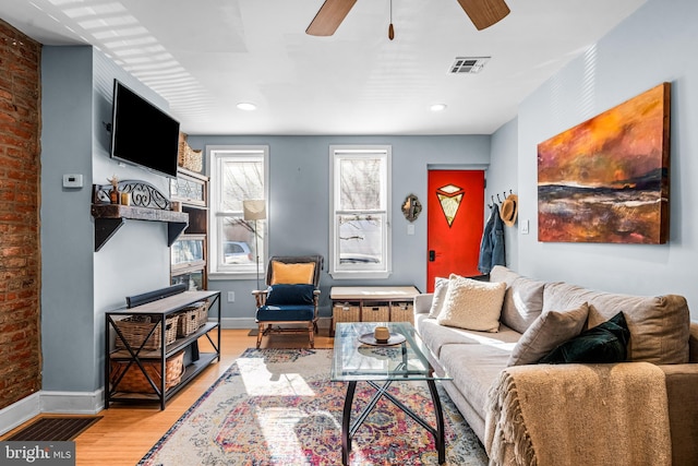 living area featuring visible vents, baseboards, brick wall, light wood finished floors, and a ceiling fan